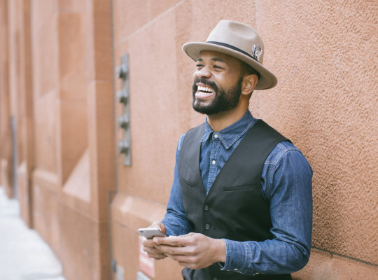 a man with a fedora and a mobile phone smiling