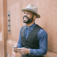 a man with a fedora and a mobile phone smiling