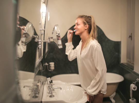 Young blond woman brushing her teeth in front of the mirror