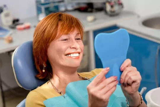 Woman sitting in a dental chair, looking in a hand mirror